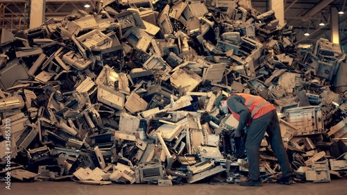 Electronic garbage recycling factory. Landfill inspector is throwing waste debris into a pile photo