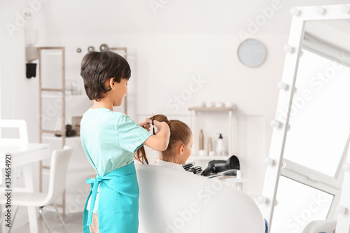 Cute little hairdresser working with client in salon