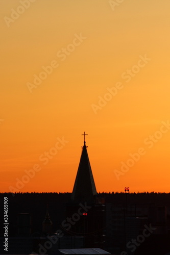 Sun below the horizon and the roof of the church with a cross on the background fiery dramatic orange sky at sunset or dawn backlit by the sun. Place for text and design. © Stanislav