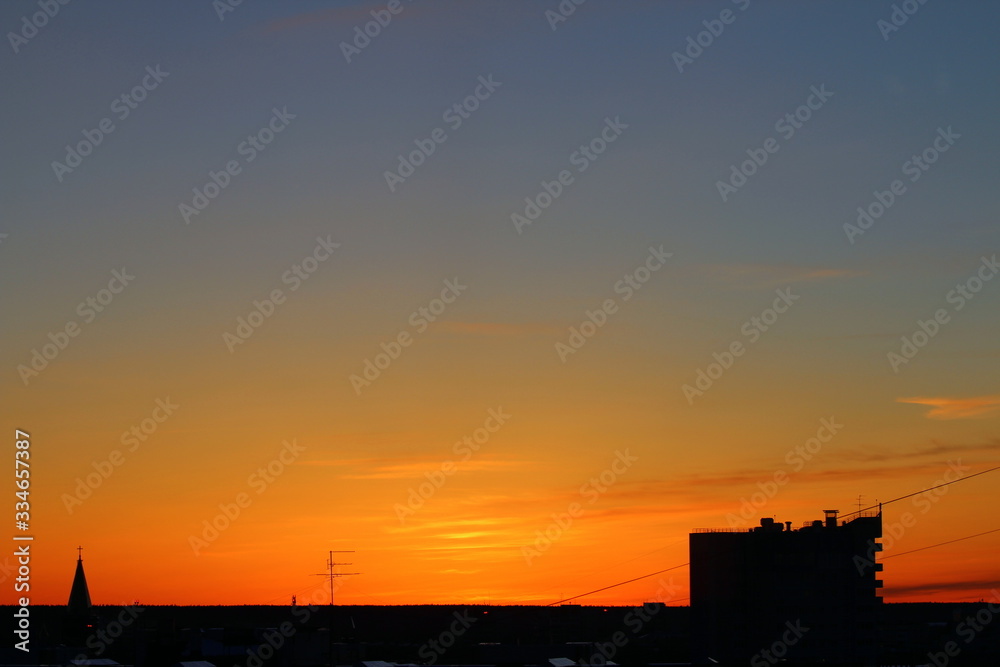 Sun below the horizon and television antenna, roof of a multi-storey urban building in the background fiery dramatic orange sky at sunset or dawn backlit by the sun. Place for text and design.