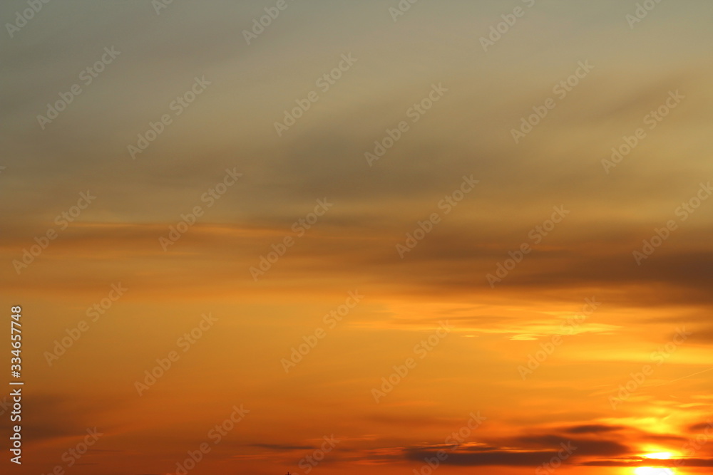 Sun below the horizon and clouds in the fiery dramatic orange sky at sunset or dawn backlit by the sun. Place for text and design.