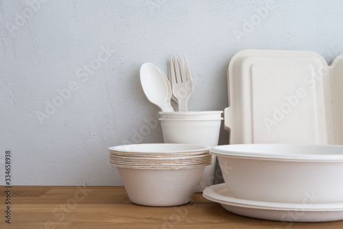 Natural eco-friendly disposable utensils (fork, spoon, dish plate, bowl, cup and fast food box container) made of fiber of bagasse and bamboo on wooden table with white wall background. Save the earth photo