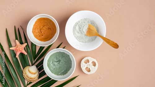 Homemade clay mask recipe concept. Top view cosmetic facial masks in bowls and tropical leaf on peach background. Face skin care, spa products, beauty treatment