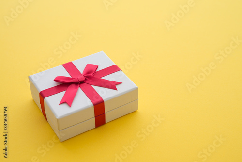Fototapeta Naklejka Na Ścianę i Meble -  Top view of white gift box with red bow ribbon on yellow background and copy space. Credit card reward point, cash back, bonus for special member concept. Business financial shopping sale promotion.