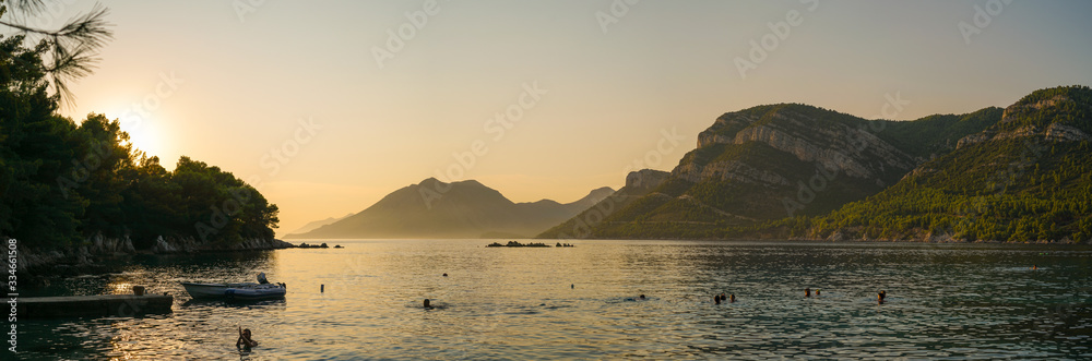 Bathing vacationers on a background of orange sunset. Quiet harbor of the Adriatic Sea near the village of Julian on the Peljesac Peninsula, Croatia