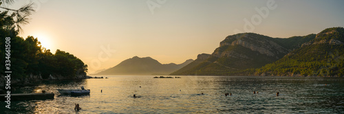 Bathing vacationers on a background of orange sunset. Quiet harbor of the Adriatic Sea near the village of Julian on the Peljesac Peninsula  Croatia