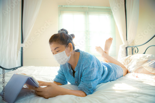 woman quarantine at home wearing protection mask and conect to internet devcie in bedroom photo