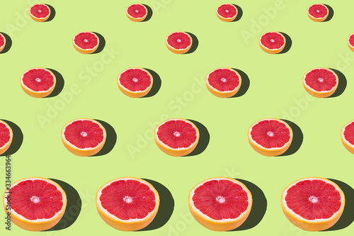 Flat lay fruit pattern of fresh grapefruit slices on green background.