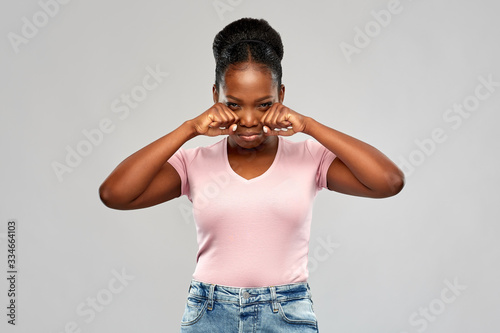 emotion, expression and people concept - sad african american woman making crying gesture or wiping tears over grey background