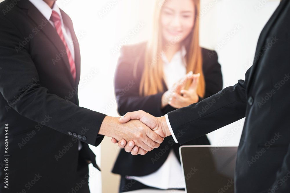closeup of asian businessmen shaking hands in partnership and business deal, business woman clapping in the background, working together in teamwork planning strategies to become successful