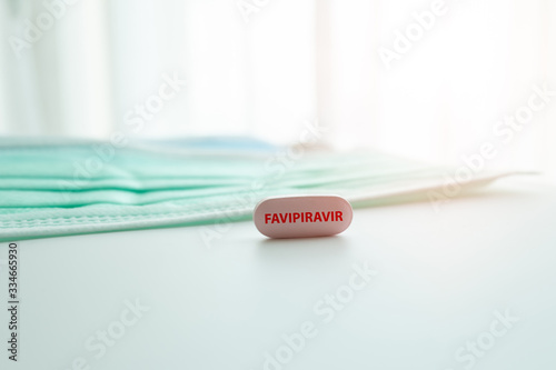Favipiravir, Avigan tablet drug medicine treatment for antivirus drug to fight Corona virus or Covid-19 on white table with green face mask background. Pandemic Protection Concept. photo