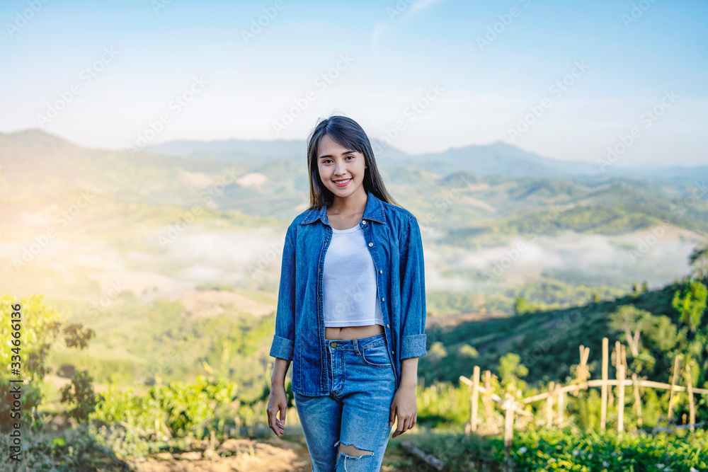Beautiful asian tourist traveler girl on holiday adventure traveling on the mountains, walking along the path smiling in the morning sunrise and misty mountains view wearing a denon jacket and jeans Beautiful asian tourist traveler girl on holiday adventure traveling on the mountains, walking along the path smiling in the morning sunrise and misty mountains view wearing a denon jacket and jeans