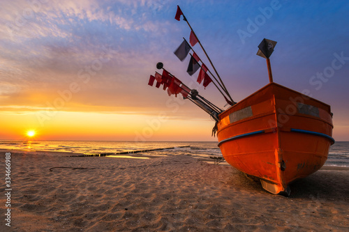 Obraz na plátně Colorful fishing boat on a sandy sea beach during a beautiful sunset