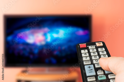 Caucasian man watching esports or concert on TV at home. Changing channels and adjusting volume with television remote control. 