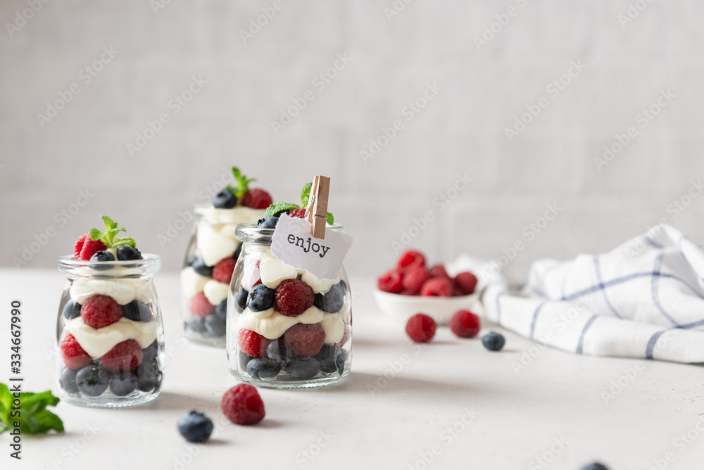 Fresh berry trifle. Raspberry and blueberry parfait with cheese cream and mint served in glass jars on white background. Summer dessert. Confectionery menu. Copy space