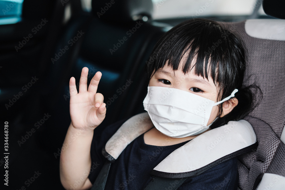 little girl in car wearing protective mask, protection from surrounding airborne transmission, concept of isolation from people, staying safe traveling to home from pandemic of corona virus COVID-19