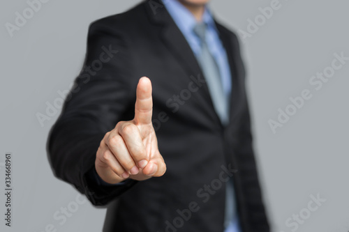 closeup concept of a male asian businessman standing pointing up a finger, wearing black suit, shirt and tie, representing interaction in technology within business industry, with grey flat background