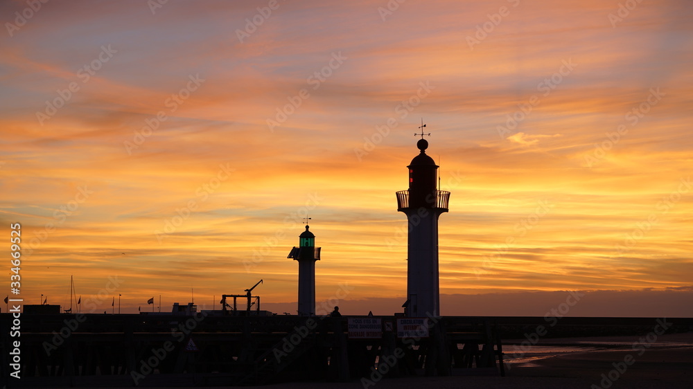 Dock of Trouville-sur-Mer, Normandy, France at sunset; orange sky and lighthouses