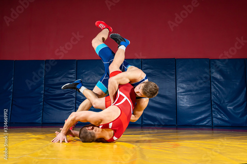 Two strong wrestlers in blue and red wrestling tights are wrestlng  on a wrestling carpet in the gym. Young man doing grapple. © Виталий Сова