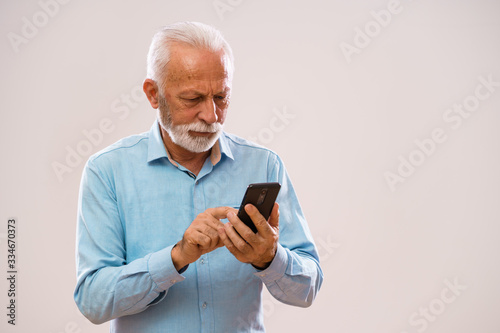 Portrait of senior man who is messaging on smartphone. © djoronimo