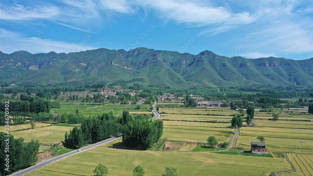 Curved road in rural fields, clear sunny summer, green mountains and village