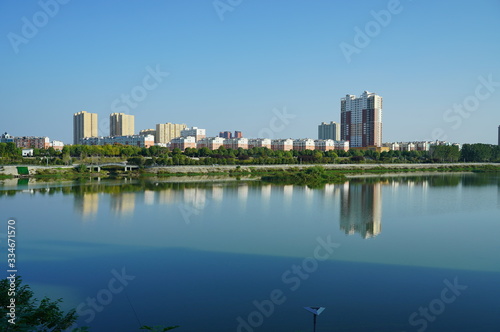 Cityscape by the river under blue sky  buildings reflecting on peaceful water