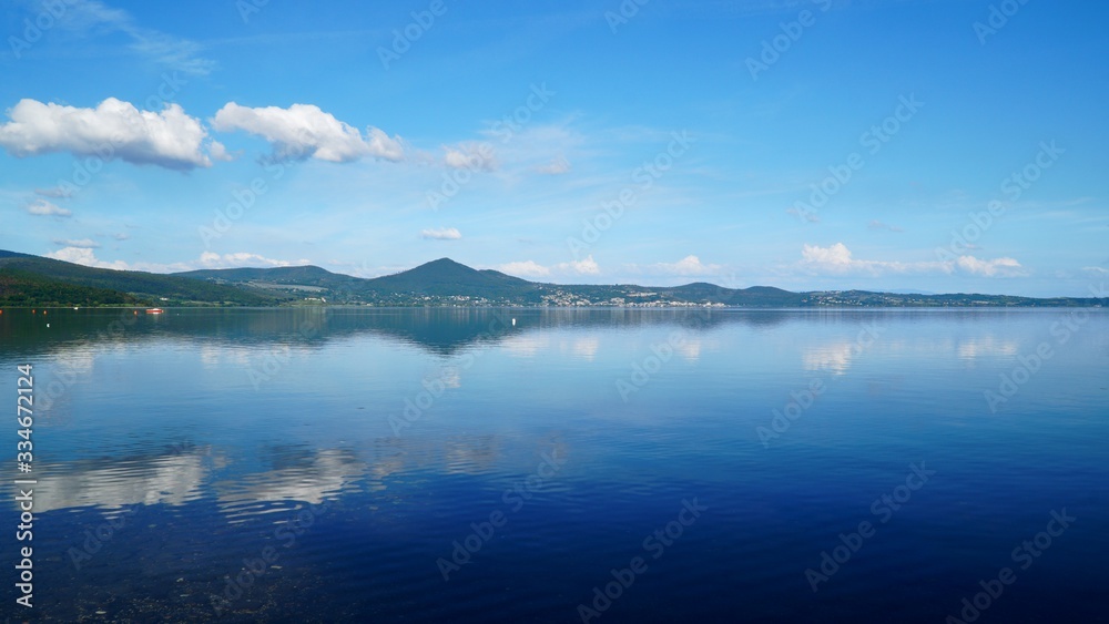 Panorama of Lake Bracciano in Roma of Italy under blue sky. White clouds and mountains reflecting on the lake