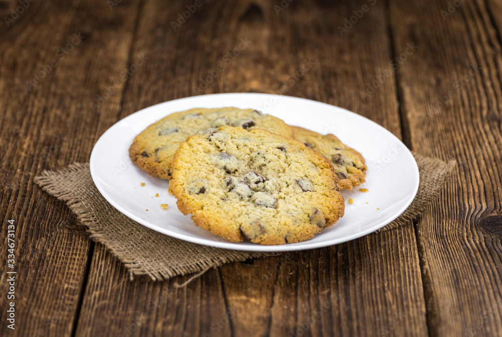Fototapeta premium Old wooden table with fresh Chocolate Chip Cookies (close-up shot; selective focus)