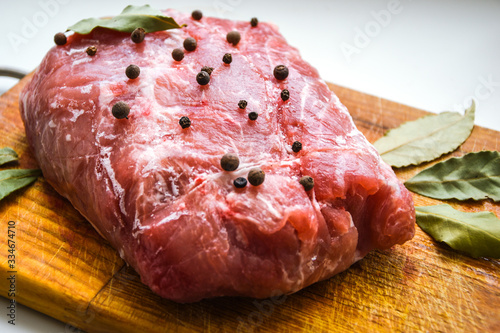 Raw pork shoulder with spices. Bay leaf, On a wooden background, close up, black pepper over a fresh raw piece of meat in spices photo