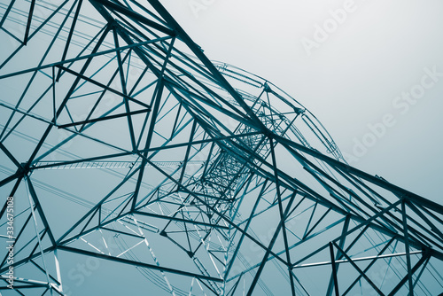Abstract pattern from bottom view of high voltage pole power transmission tower with clear sky sunny day background in monochrome tone. Green energy, environmental conservation concept.