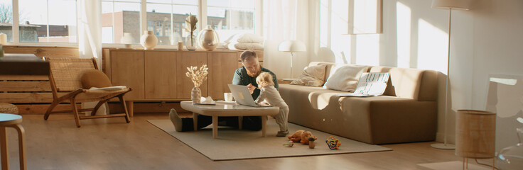 Father working from home alone, feeding his daughter in front of laptop. Stay home, quarantine remote work