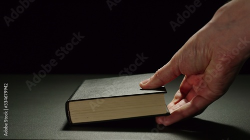 Man Putting A Thick Black Book On A Black Surface