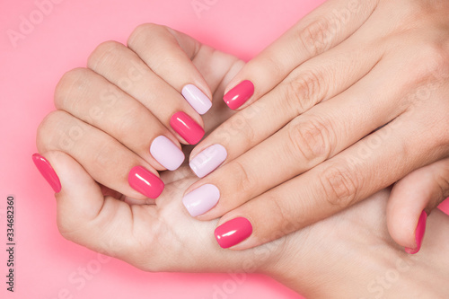 Closeup photo of two female hands and fingers manicured. Fingernails with fresh professional spring or summer naildesign isolated on pastel pink background. Painted nails with modern gel-polish.