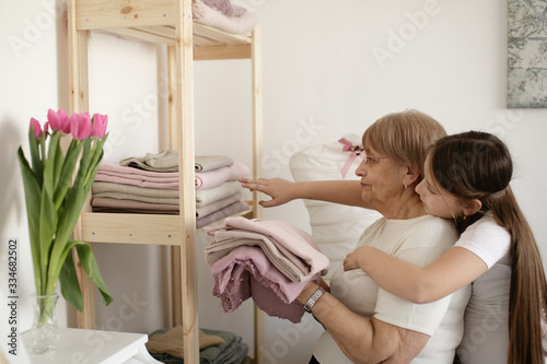 Grandmother with granddaughter are storing clothes at home together