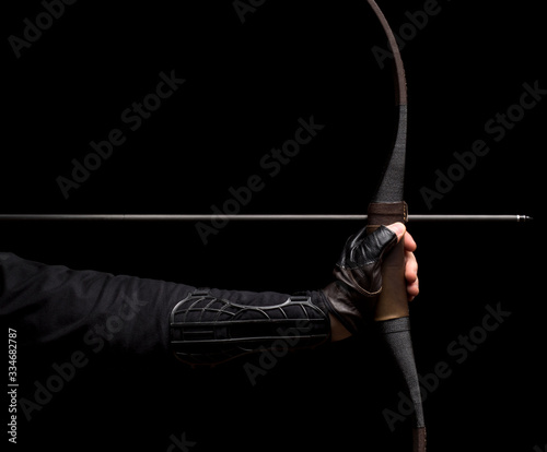 Archer's hand with bow before shooting on black background (ID: 334682787)