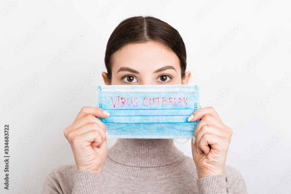 Portrait of pretty woman holding medical mask with virus outbreak text in hands at white background. Coronavirus concept. Respiratory protection Portrait of pretty woman holding medical mask with virus outbreak text in hands at white background. Coronavirus concept. Respiratory protection
