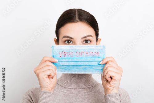 Portrait of pretty woman holding medical mask with virus outbreak text in hands at white background. Coronavirus concept. Respiratory protection