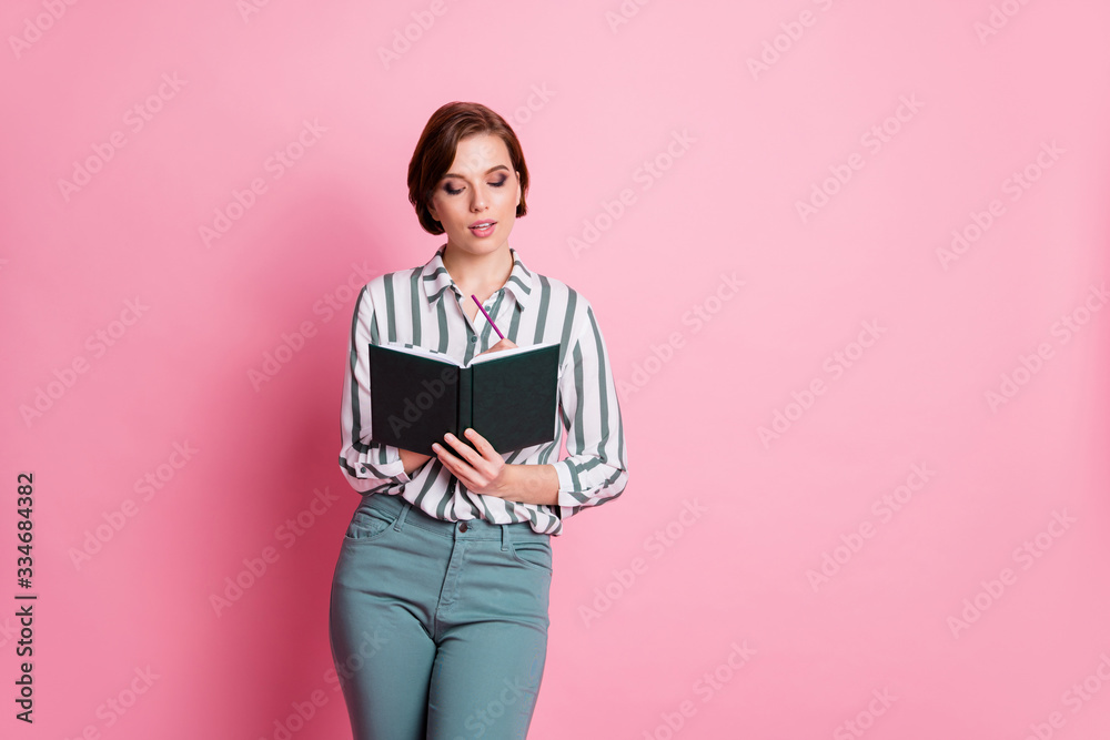 Portrait of focused intelligent girl write notes in copy book work worker on review wear stylish clothes isolated over pink color background Portrait of focused intelligent girl write notes in copy book work worker on review wear stylish clothes isolated over pink color background
