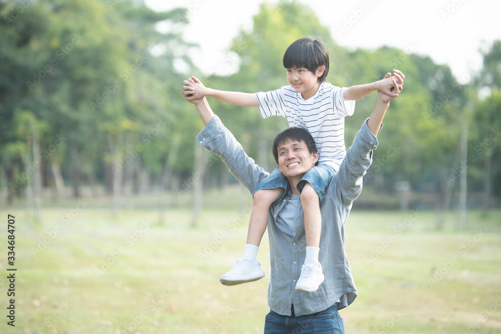 Happy family, Young father with his little child sitting on father's shoulders in summer in public park with beautiful sunset, spending and relaxing time on the weekend concept