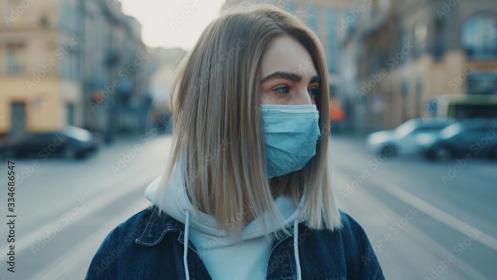Fototapeta premium Close up view of a sad young caucasian woman wearing protective mask on the street road outdoor. Concept of health and safety life N1H1 covid19 coronavirus virus protection pandemic cars city