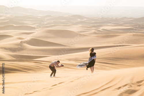 A photographer works with a woman model in the desert. A man photographs a young woman in the sands of the desert an advertising shoot for a magazine