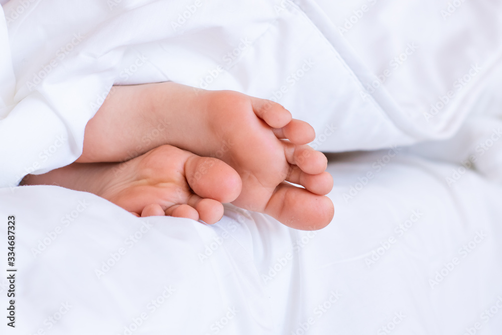 Child feet under the clear soft white blanket. Tenderness of morning dream Child feet under the clear soft white blanket. Tenderness of morning dream