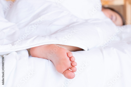 Child feet under the clear soft white blanket. Tenderness of morning dream