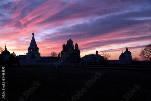 The black silhouette of the monastery against the background of a bright multicolored sunset.