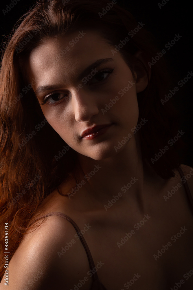 Fototapeta premium Portrait of a young curly girl in a dark studio