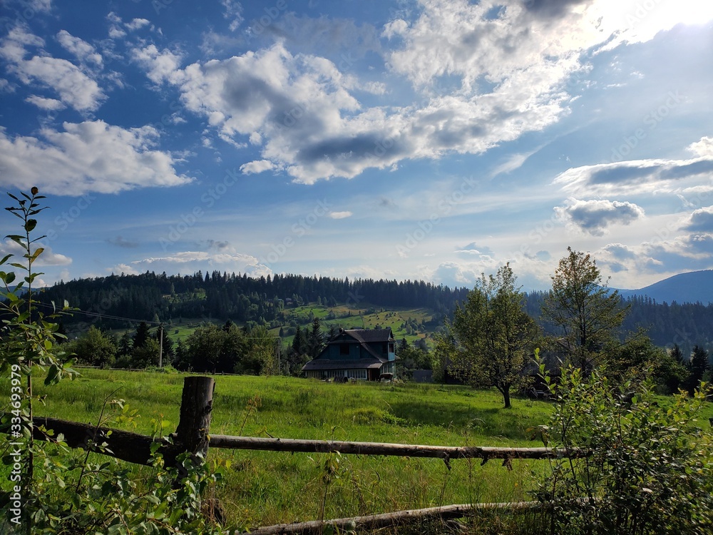 A beautiful scenery of Carpathian mountains with small houses, trees, fields, and roads in the summertime.