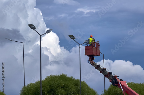 workers in lift bucket repair street light pole with double head and change the lighting to diode