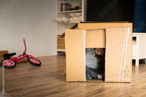 Little child girl sitting in a cardboard playhouse while moving in a new house. photo