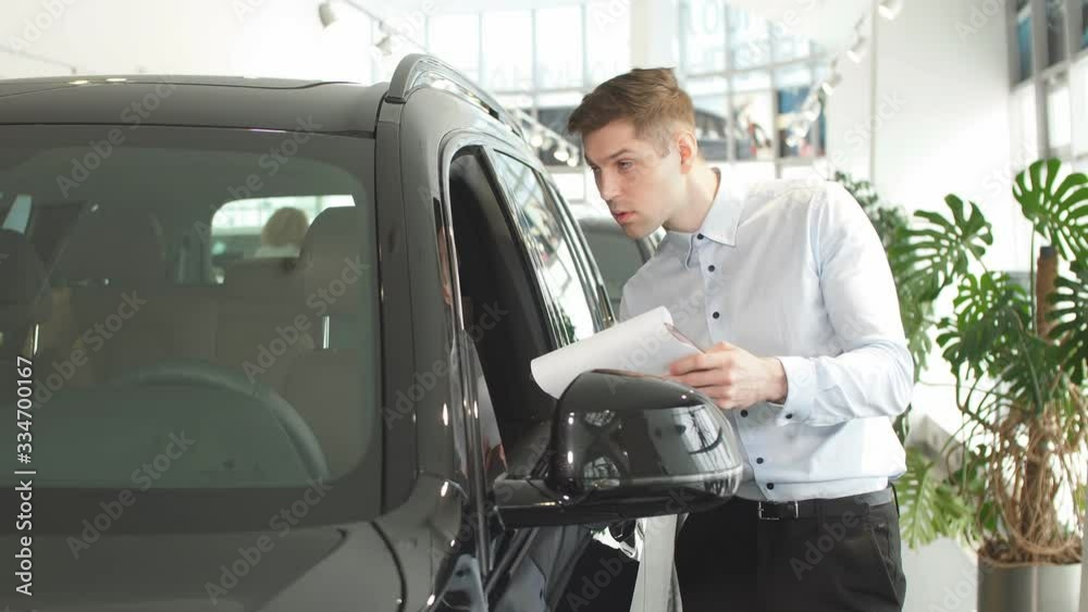 Young handsome caucasian guy examining new car before making purchase. perfect auto in dealership. Man want to buy it.