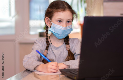 Distance learning online education.School girl in medical mask does homework on laptop at home.Quarantine